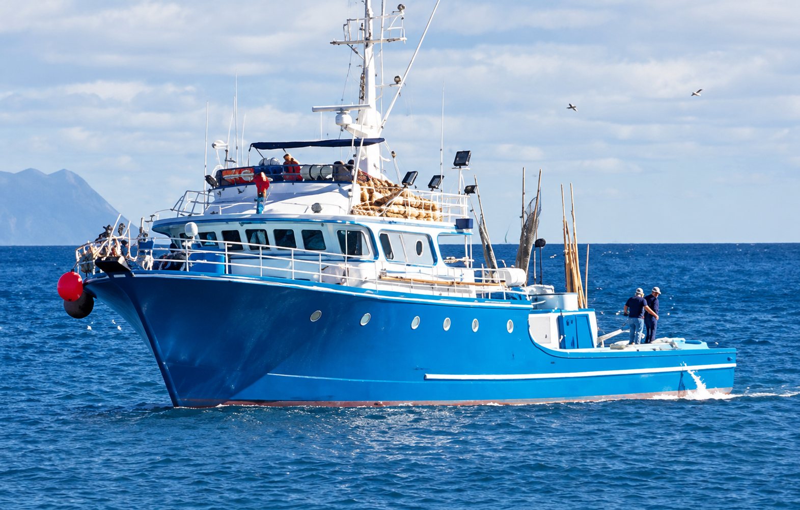Chalutier bleu et blanc en mer, près de la côte, sous un ciel nuageux